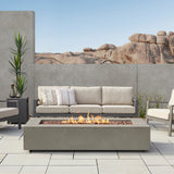 Real Flame Aegean 70 inch rectangle propane fire pit table in Mist Gray – shown on a patio with outdoor sofa (stock photo)