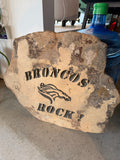 Front of the "BRONCOS ROCK!" engraved sandstone stone showing the irregular natural edge, lichen-like markings and the small artist-signed RK mark