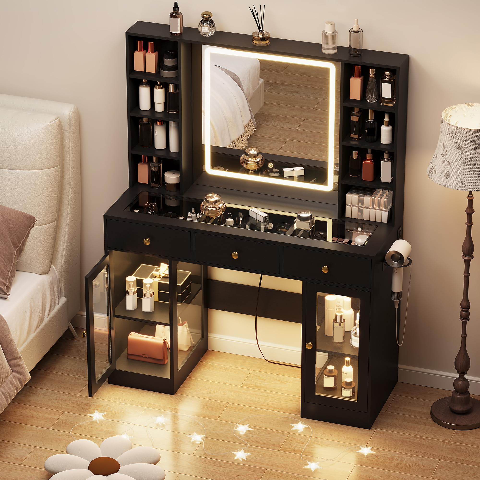 Black vanity desk with lighted mirror and glass cabinets in a bedroom – angled view (manufacturer image)